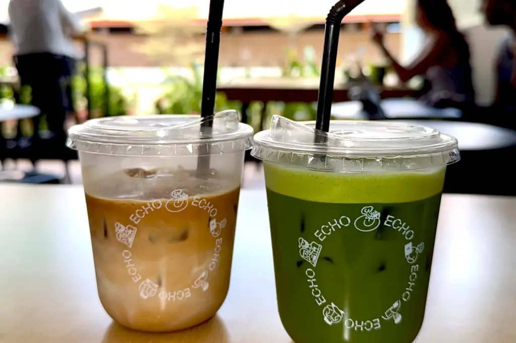 Two iced beverages—a signature latte and a vibrant green matcha drink—in branded Echo Cafe cups, showcasing the cafe's popular drink menu.