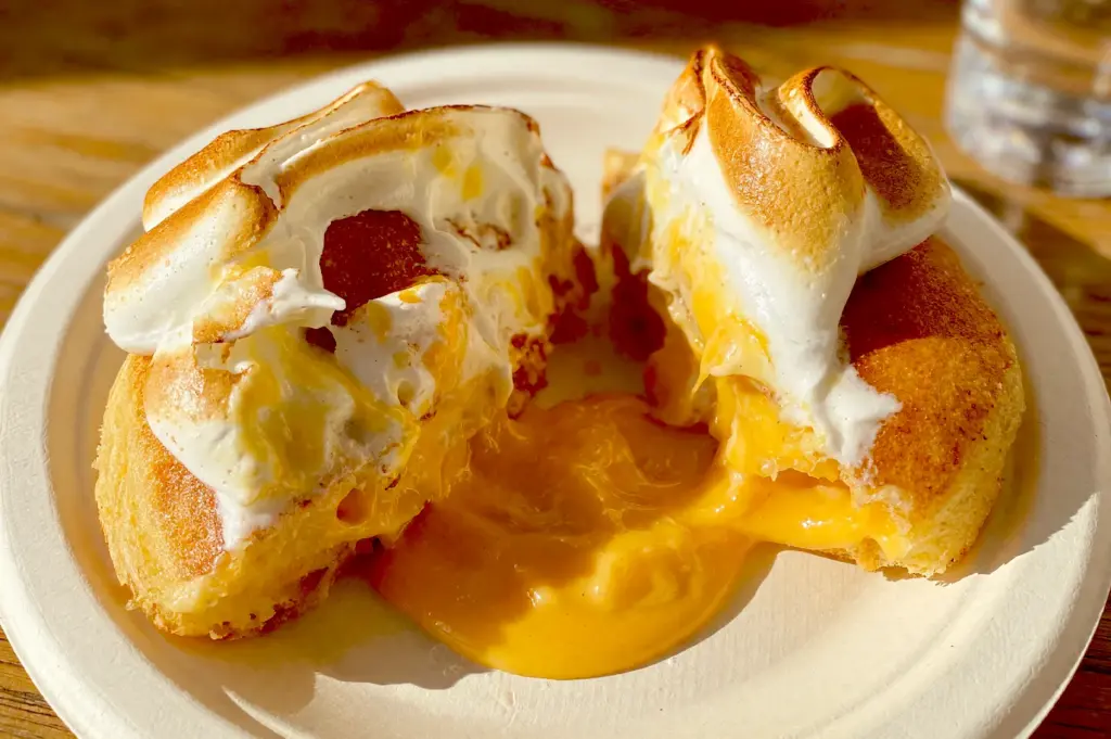 Close-up of a signature Burnt Ends Bakery doughnut split in half, revealing a rich, flowing lemon custard filling topped with toasted marshmallow meringue.