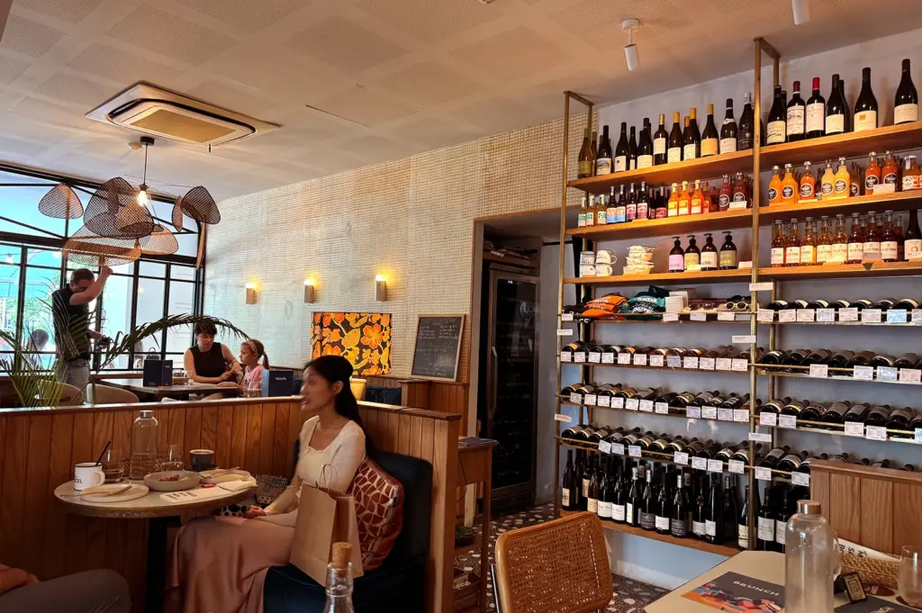 A view of the dining area at Merci Marcel Club Street, showcasing tall shelves stocked with curated French wines and a stylish, relaxed dining environment.