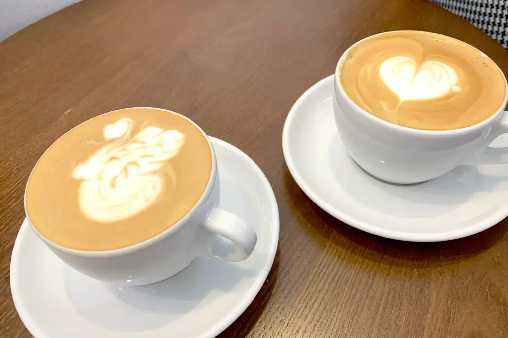 Two elegant cups of decaf latte, one with swan latte art and the other with a heart, served on a cafe table, typical of specialty coffee shops in Singapore.