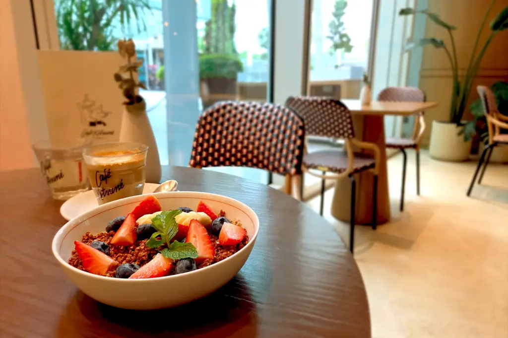 A healthy and colorful acai granola bowl served with fresh berries, captured alongside a specialty drink at a table in the stylish Café Kitsuné Singapore.