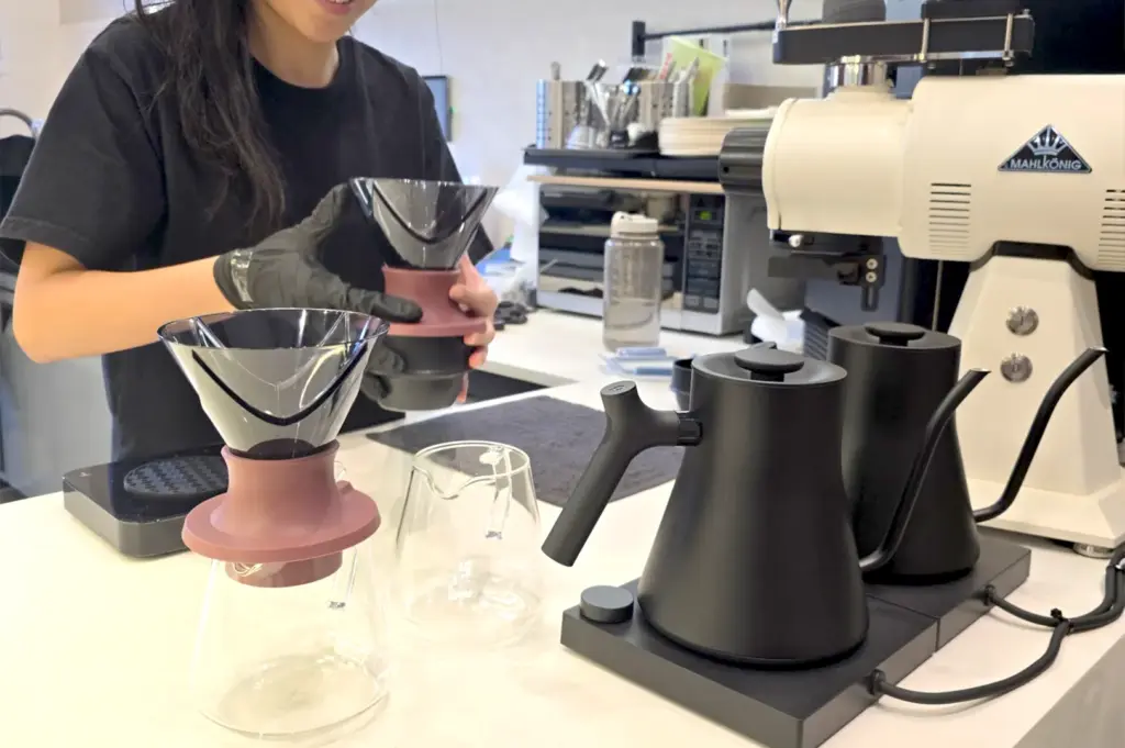 A barista at Echo Cafe in Singapore carefully preparing a hand-poured coffee using professional brewing equipment and sleek black kettles.