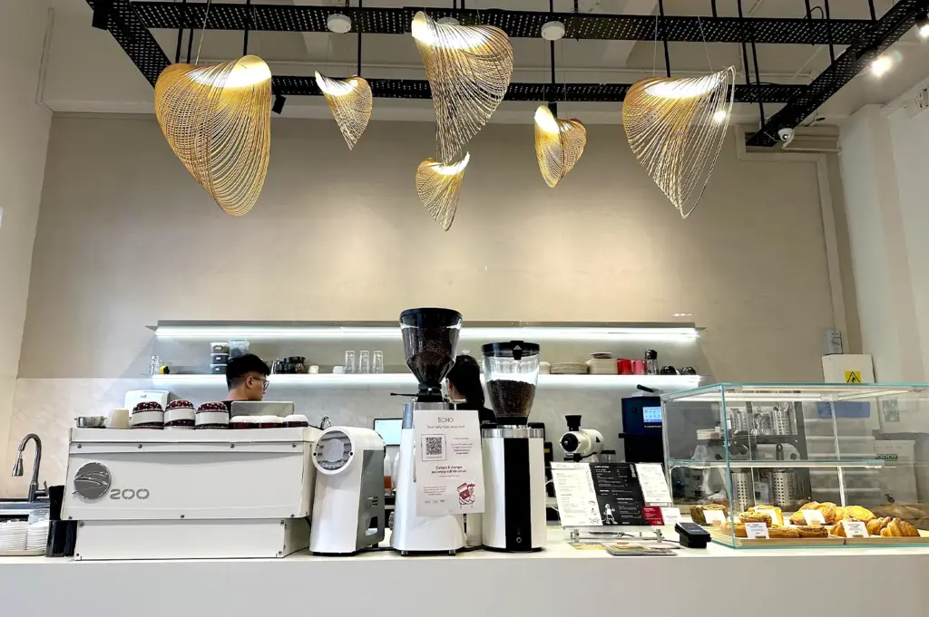 The bright and modern interior of Echo Cafe, featuring stylish, abstract golden pendant lighting, a clean white counter, and professional coffee brewing machinery.