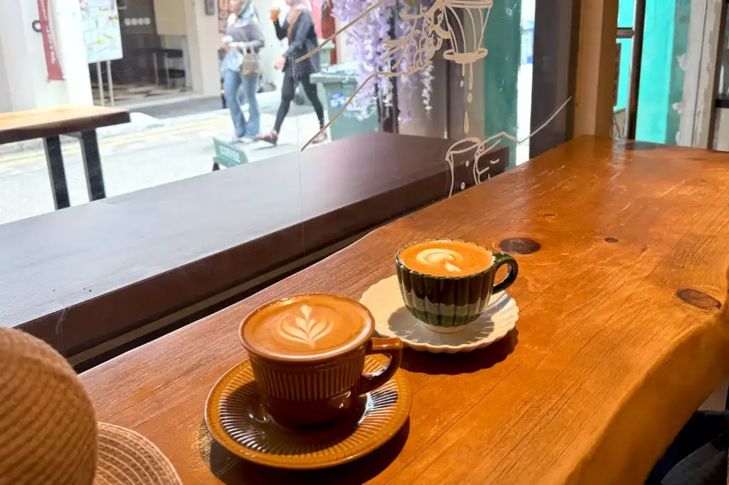 Two artistic cups of decaf latte placed on a wooden table by a window in a Singapore cafe, capturing the ambiance of enjoying a decaf coffee.