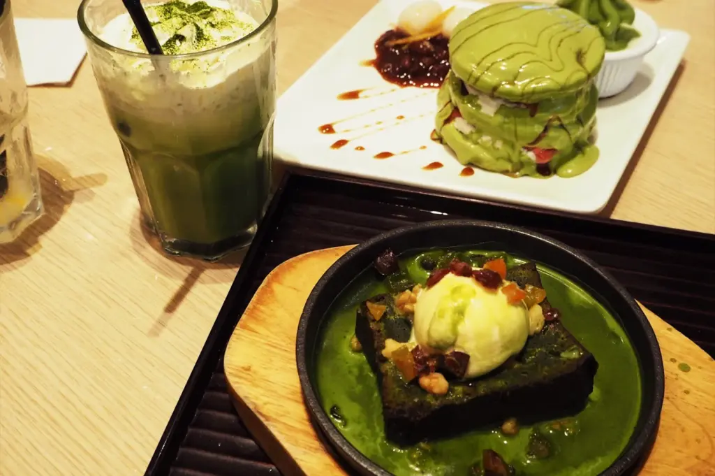 A vibrant selection of Japanese-inspired matcha desserts at Maccha House, including a green tea latte, a matcha layered pancake stack, and a sizzling matcha brownie with ice cream.