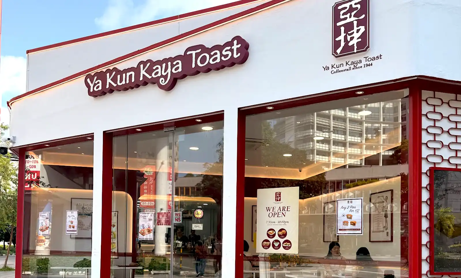 Exterior storefront of a Ya Kun Kaya Toast traditional coffee stall in Singapore, featuring white and maroon branding and large glass windows.