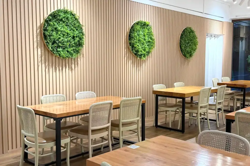 A bright interior section of The Garden Slug featuring light wood tables, matching chairs, and circular green plant wall decorations.