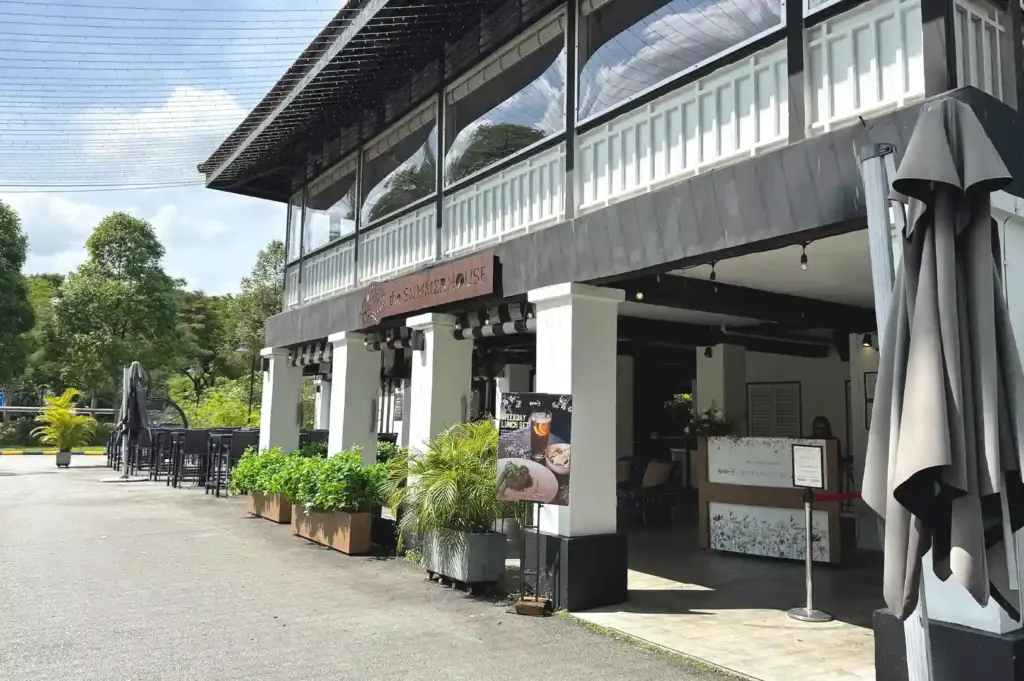 An exterior daytime view of The Summerhouse building in Singapore, surrounded by lush potted plants and outdoor seating.