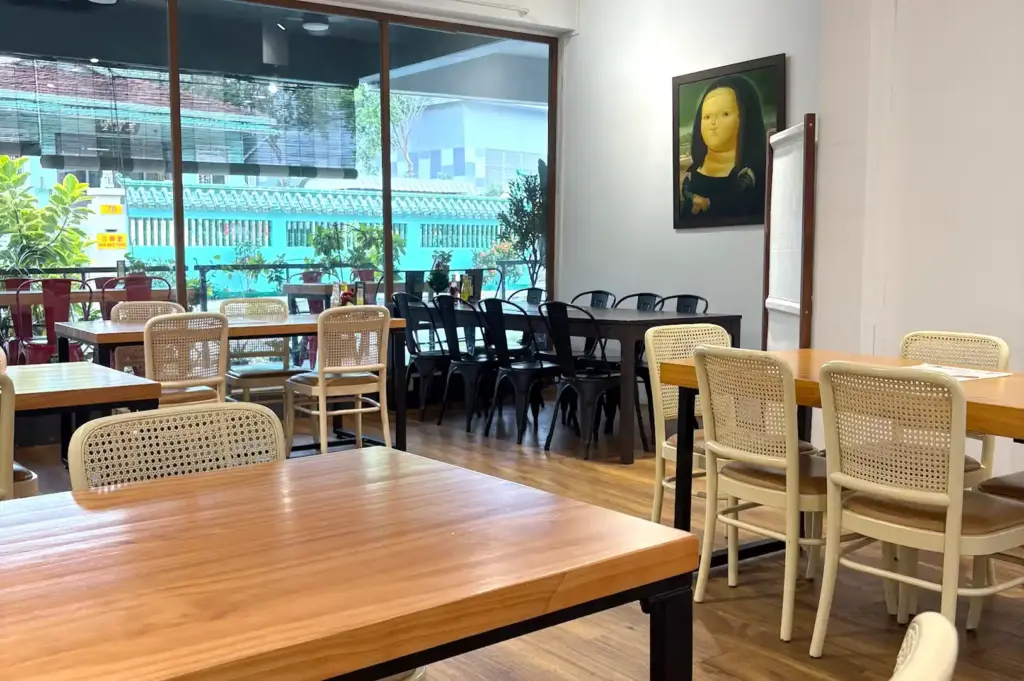 The spacious dining room at The Garden Slug cafe, highlighting wooden tables, woven-back chairs, and a whimsical painting on the wall.