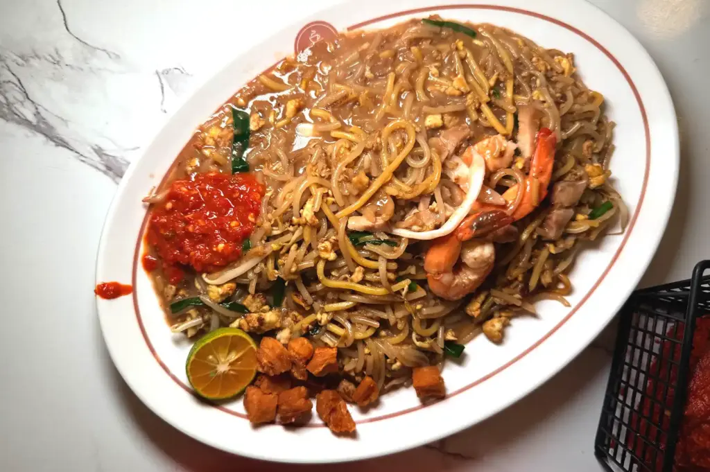 A plate of flavorful signature Hokkien mee topped with prawns, pork slices, crispy lard, and chili paste at Bao Er Cafe.