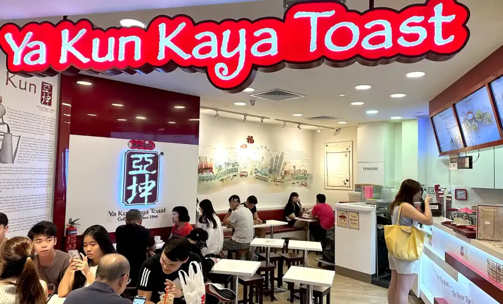 Bustling interior scene of a busy Ya Kun Kaya Toast outlet in Singapore with customers enjoying breakfast and ordering at the counter.
