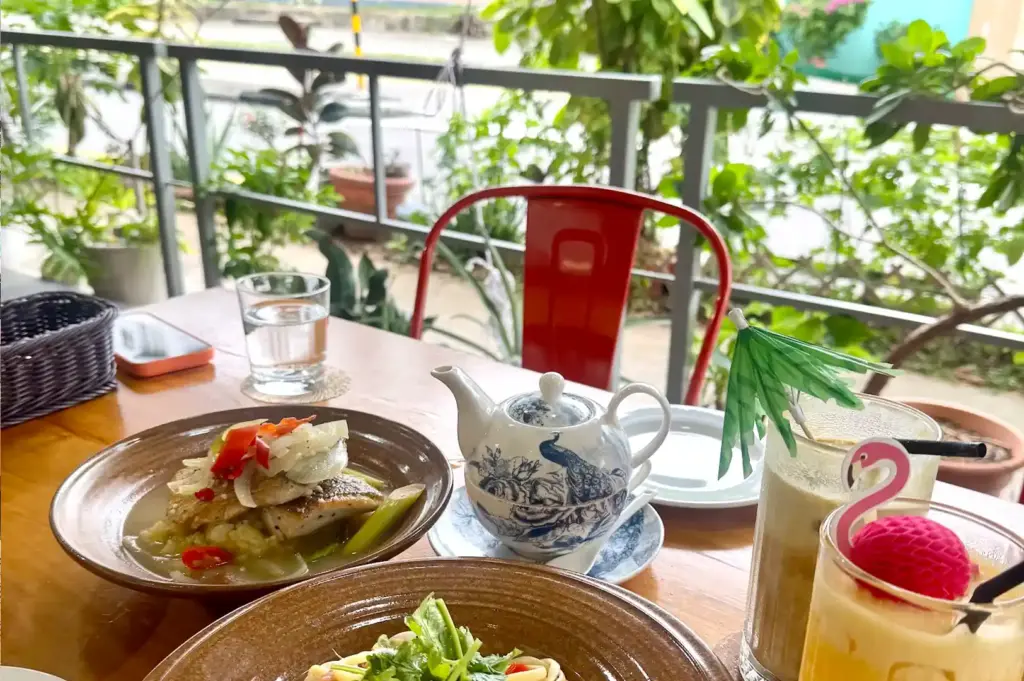 A cozy table setting at The Garden Slug featuring savory fish dishes, a patterned teapot, and tropical drinks garnished with decorative umbrellas.