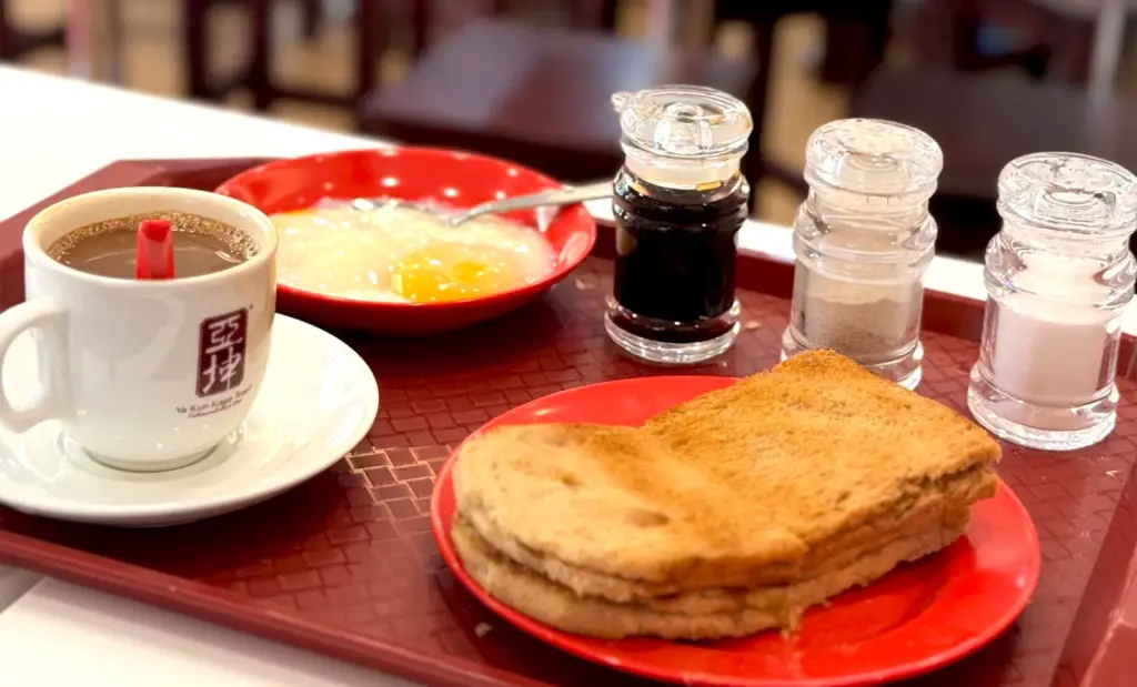 A complete traditional breakfast set at Ya Kun Kaya Toast including kaya toast, soft-boiled eggs, coffee, and condiment shakers.