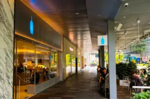 Blue Bottle Coffee exterior with its simple blue logo signage above the entrance and the interior blooming with warm yellow lights.