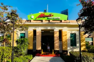 Maxwell Food Centre exterior with its distinctive green, red, and white arched signage and yellow paint surrounded by greenery in braod daylight.