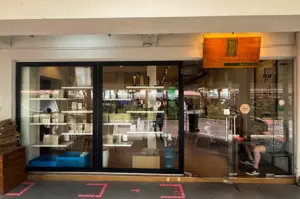 Wide angle shot Tiong Hoe Specialty Coffee exterior with glass doors and panels and a wooden, warmly lit logo signage on top of the entrance.