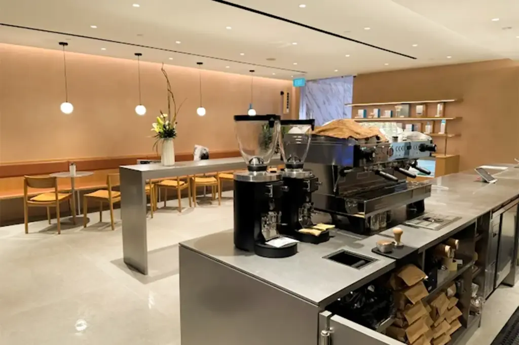 Blue Bottle Coffee interior with its clean minimalist architecture with warm themed chairs and table and the counter with coffee machines and blenders in the foreground.
