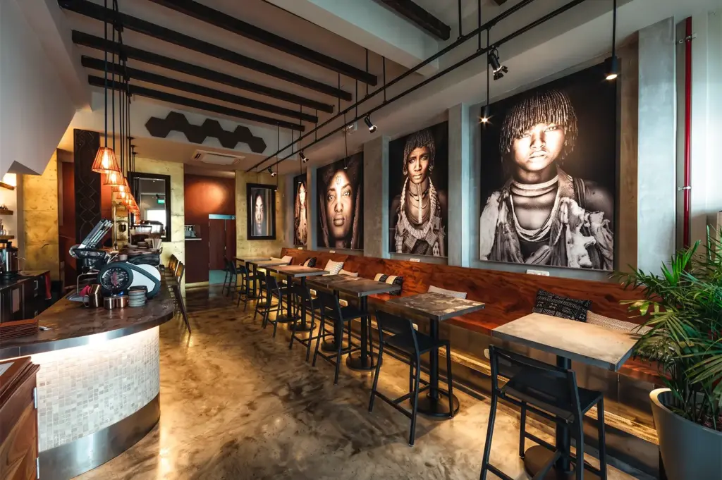 Kafe Utu interior with a warm brown and yellow cozy vibe with the dark brown wooden tables and chairs and paintings with hanging yellow lights.