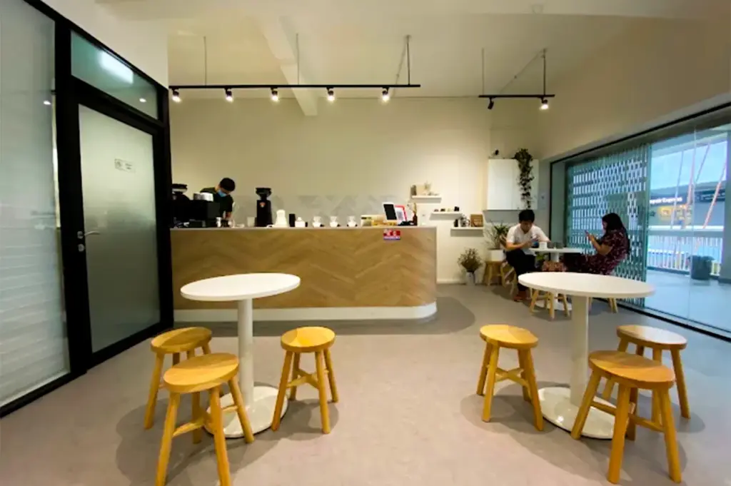 Zerah Coffee Roasters with its minimalist tables and chairs with a couple dining at a back and a staff preparing menu dishes at the counter to the left.