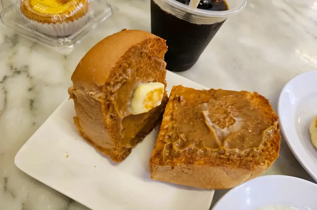YY Kafei Dian kaya bun sliced in half served on a white square plate.
