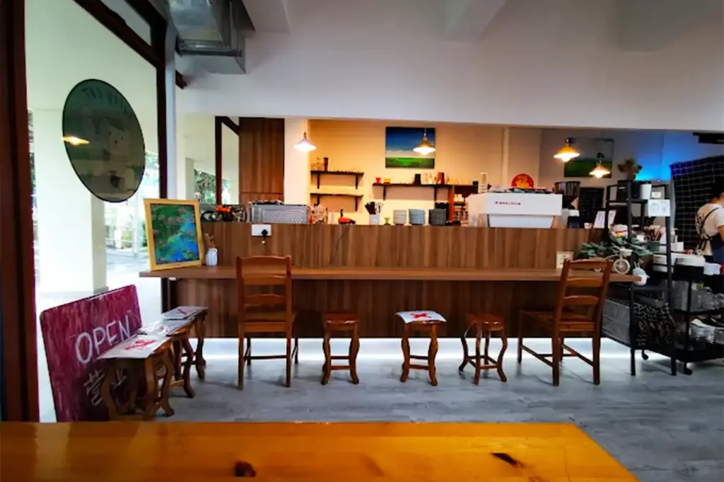 Lucky Cat Vegetarian/Vegan Cafe interior with empty chairs and tables by the counter, its white and brown colored walls and furniture surrounding the counter lighted by yellow lights above.