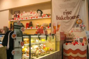 Rise Bakehouse interior counter with colorful pastries in a glass display and a banner with the brand logo on the right.