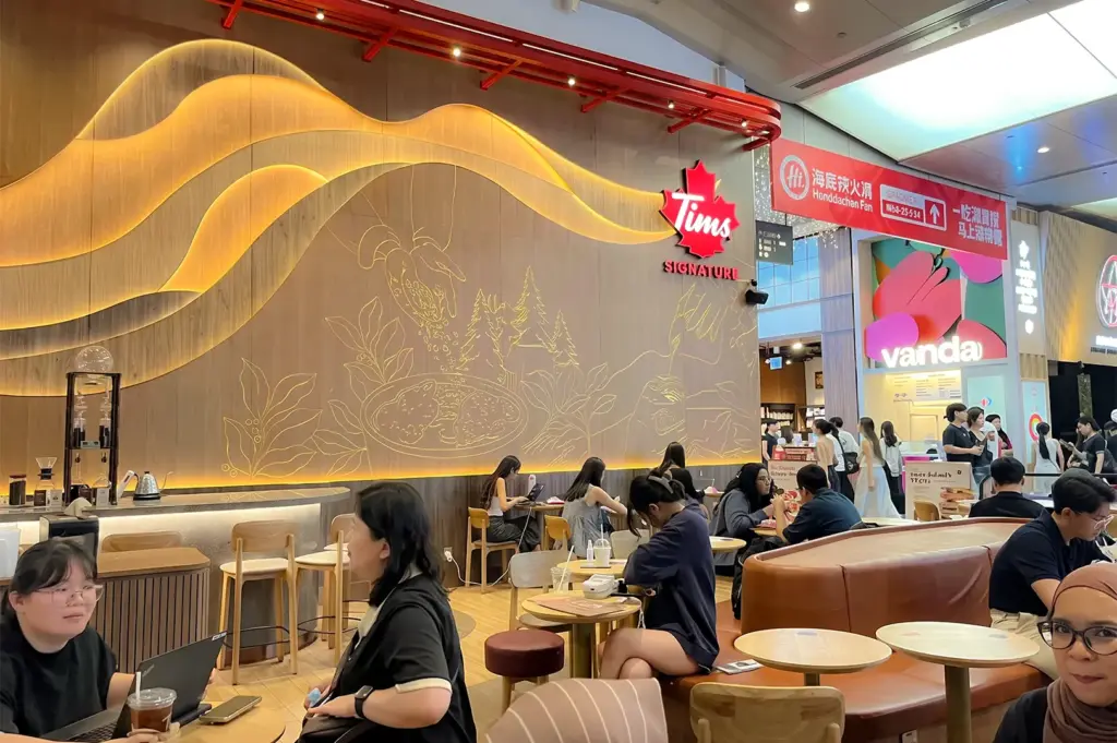 Tim Hortons interior view with a decorated wall with their logo surrounded by dining customers in brown tables and chairs.