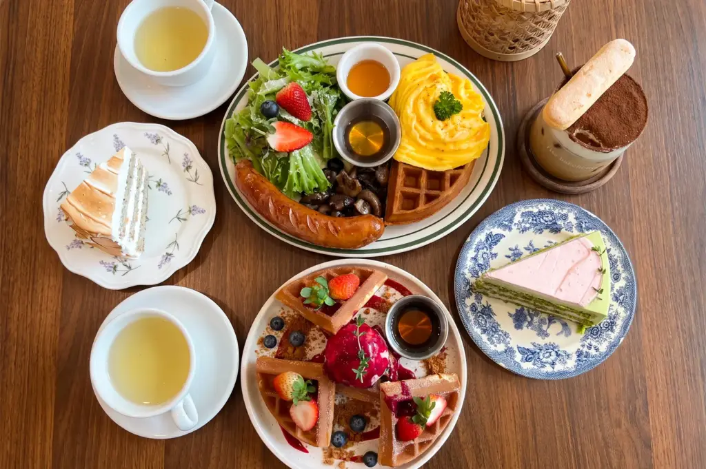 Flat lay view of Rise Bakehouse menu items including waffles, cakes, coffee, and sausages neatly arranged on top of a wooden table.