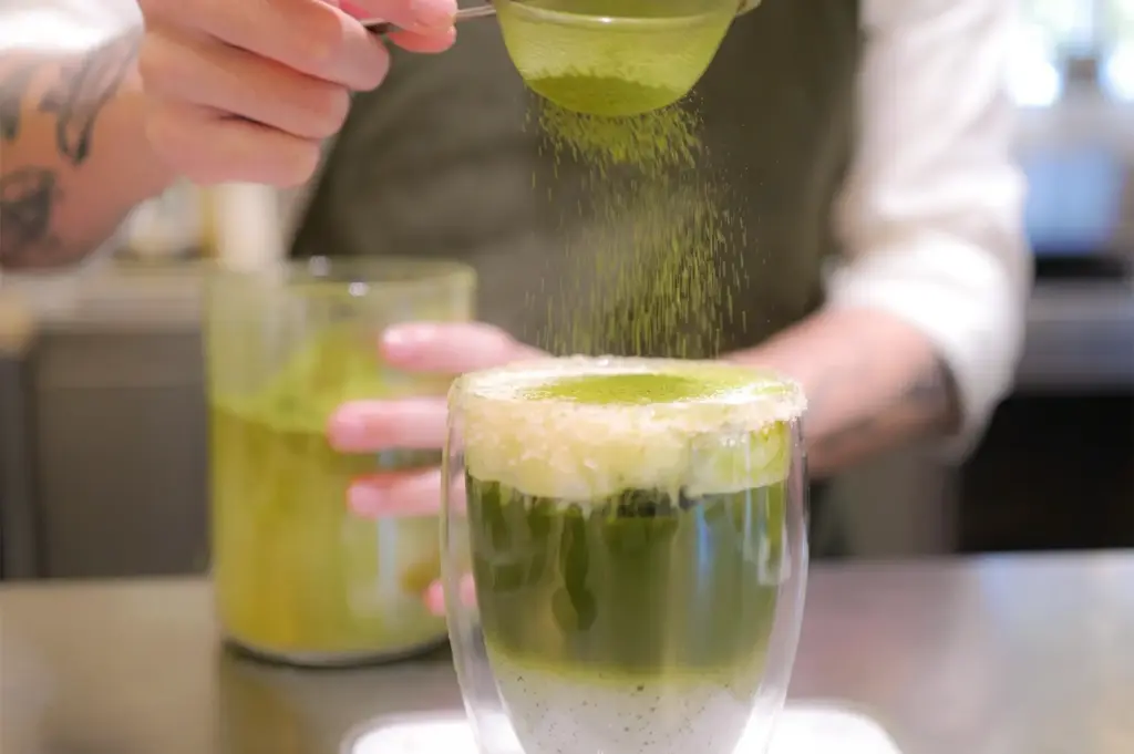 A freshly made matcha drink with powder being sprinkled on top.