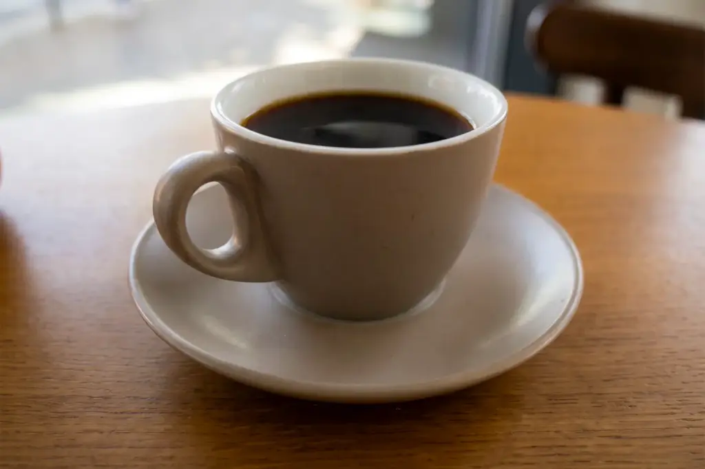 A fresh cup of kopi luwak in a white coffee cup and saucer on a brown table.